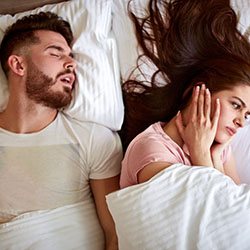 Man snoring while woman covers her ears