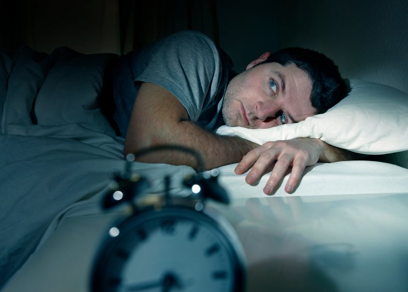 Man with sleep apnea lying awake staring at alarm clock