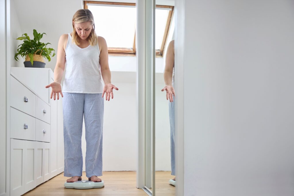 Woman standing on scale making frustrated gesture with hands