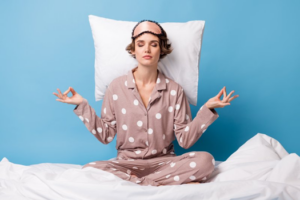 Woman sitting cross-legged on her bed with a pillow behind her head